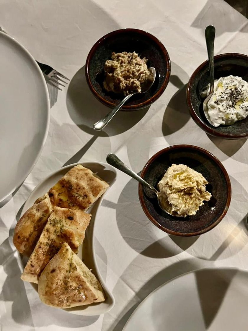 Three homemade dips in dark bowls, one of aubergine, one of yoghurt with herbs and one pale and creamy, with toasted pitta triangles
