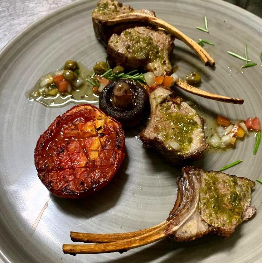 Lamb chops with a green herb crust, a grilled tomato half and a mushroom, on a grey plate