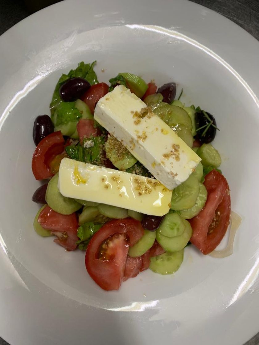 Greek salad with two slabs of feta, tomato, cucumber, olives and oregano in a white bowl