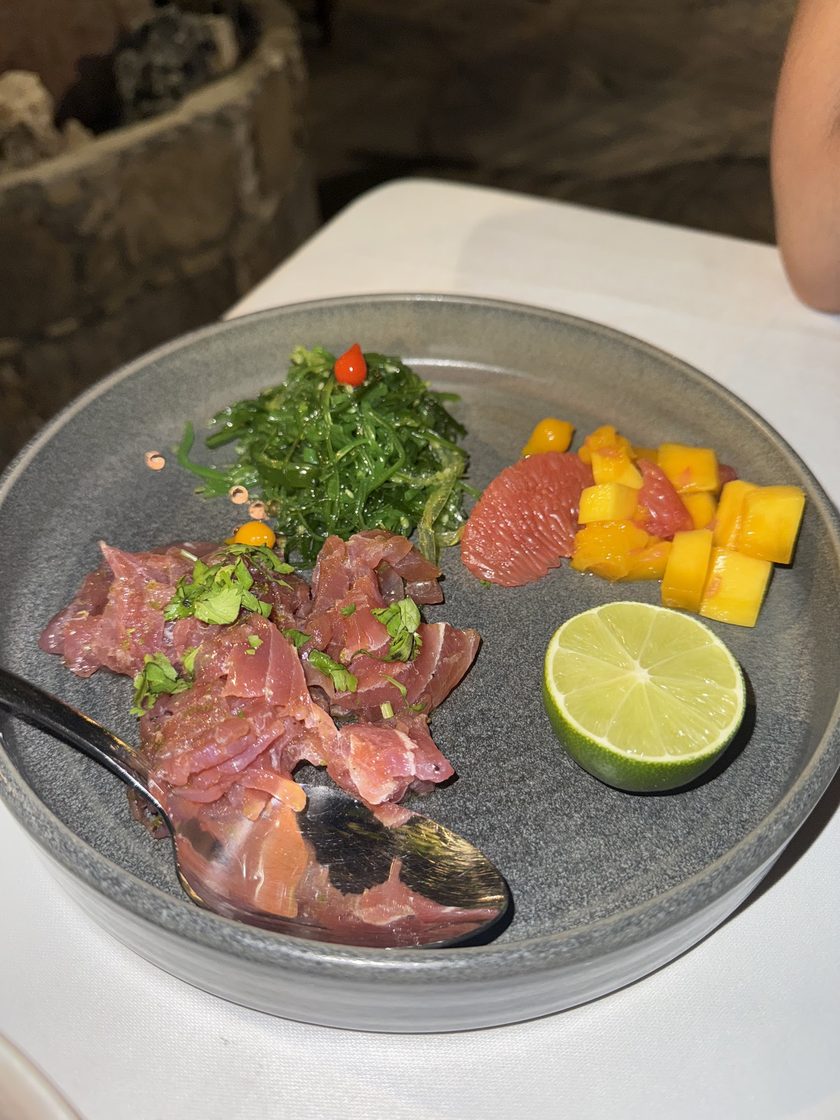 Tuna ceviche on a grey plate with seaweed salad, diced mango, grapefruit and half a lime