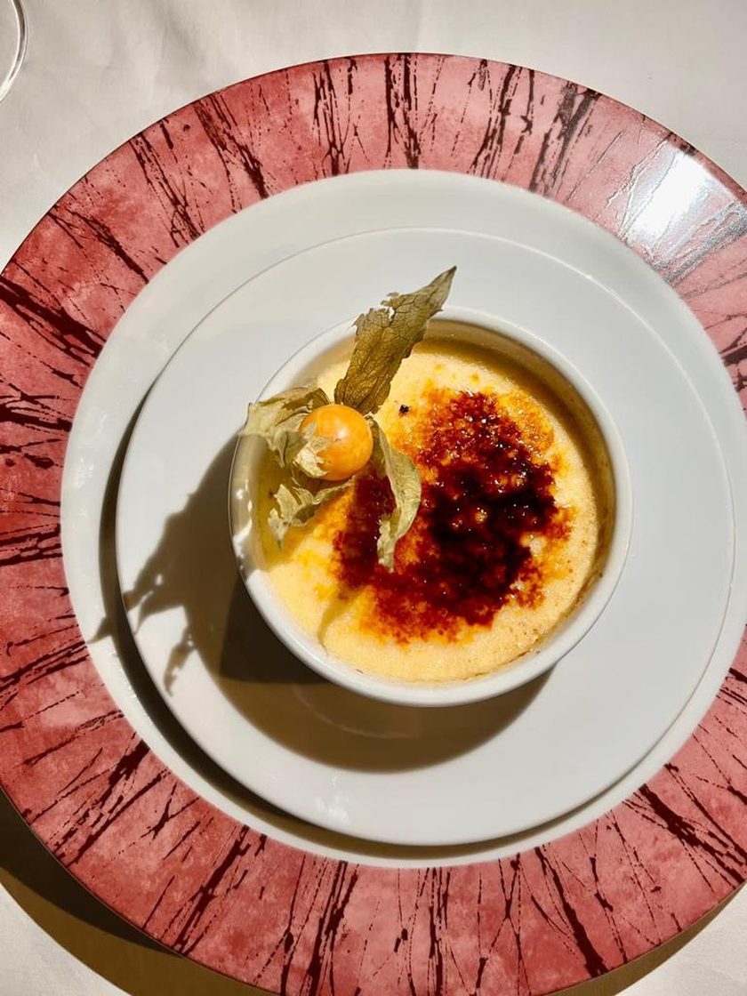 Creme brulee in a white ramekin with a physalis, on a plate with a red painted rim