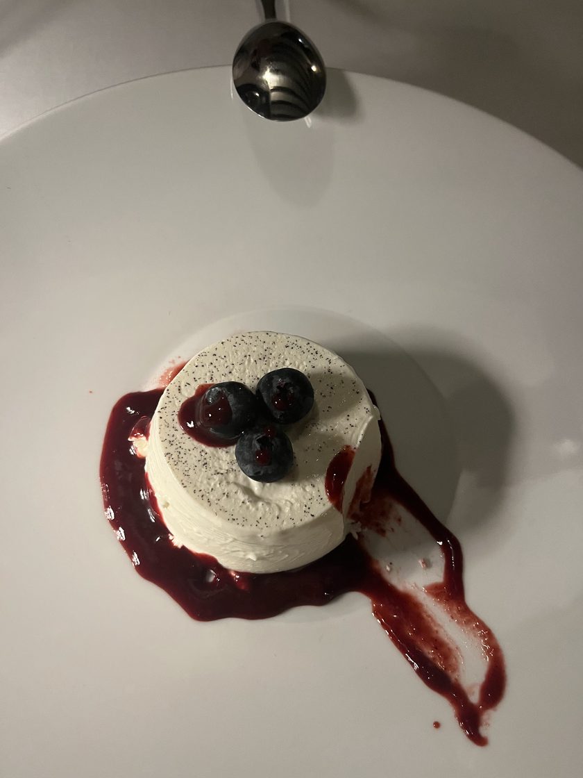 Panna cotta topped with blueberries and a dark berry sauce, on a white plate