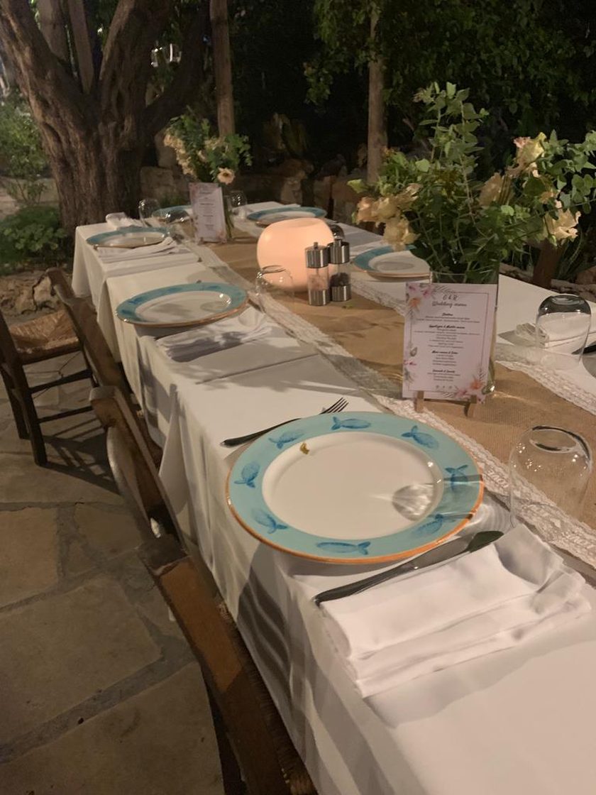 A long table laid for a party in the garden at night: blue-rimmed plates, a runner of hessian and lace, a small lamp and printed menus