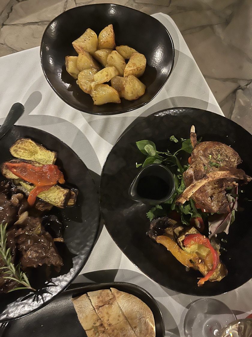 A meze spread on dark plates: grilled lamb chops, vegetables, roast potatoes and bread