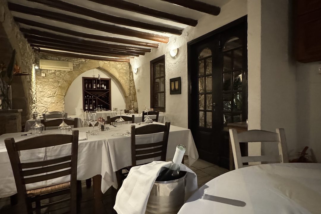 The indoor dining room at night: dark timber beams across a white ceiling, a stone arch at the far end and tables in white cloths