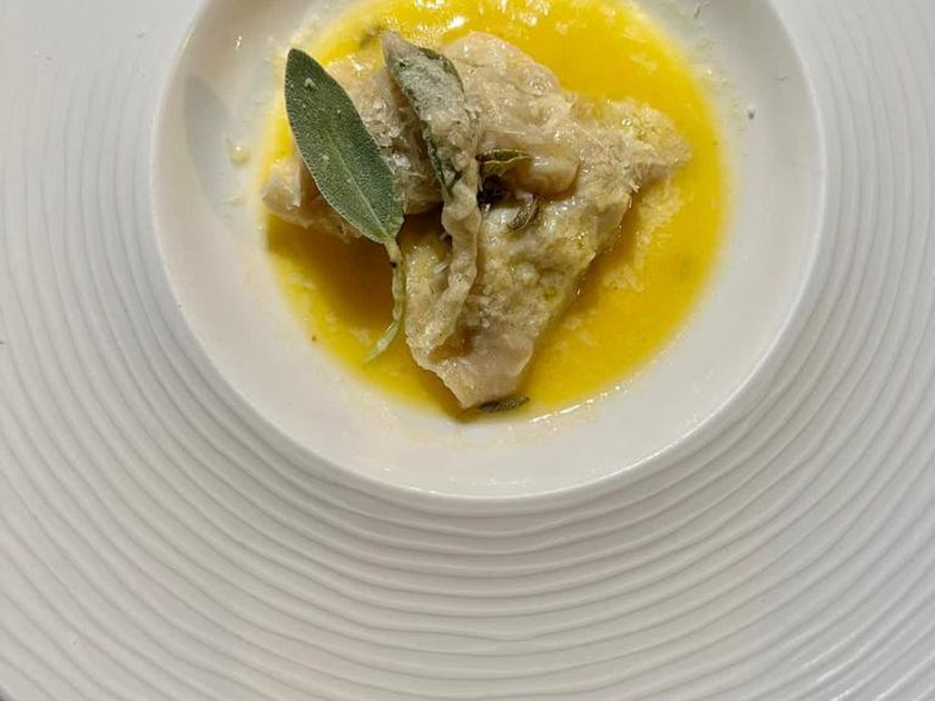 Homemade ravioli with a sage leaf in a yellow butter sauce, in a wide white bowl