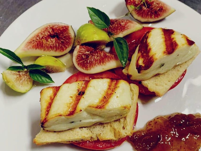 Grilled halloumi on bread over sliced tomato, with fresh figs, basil and fig jam on a white plate